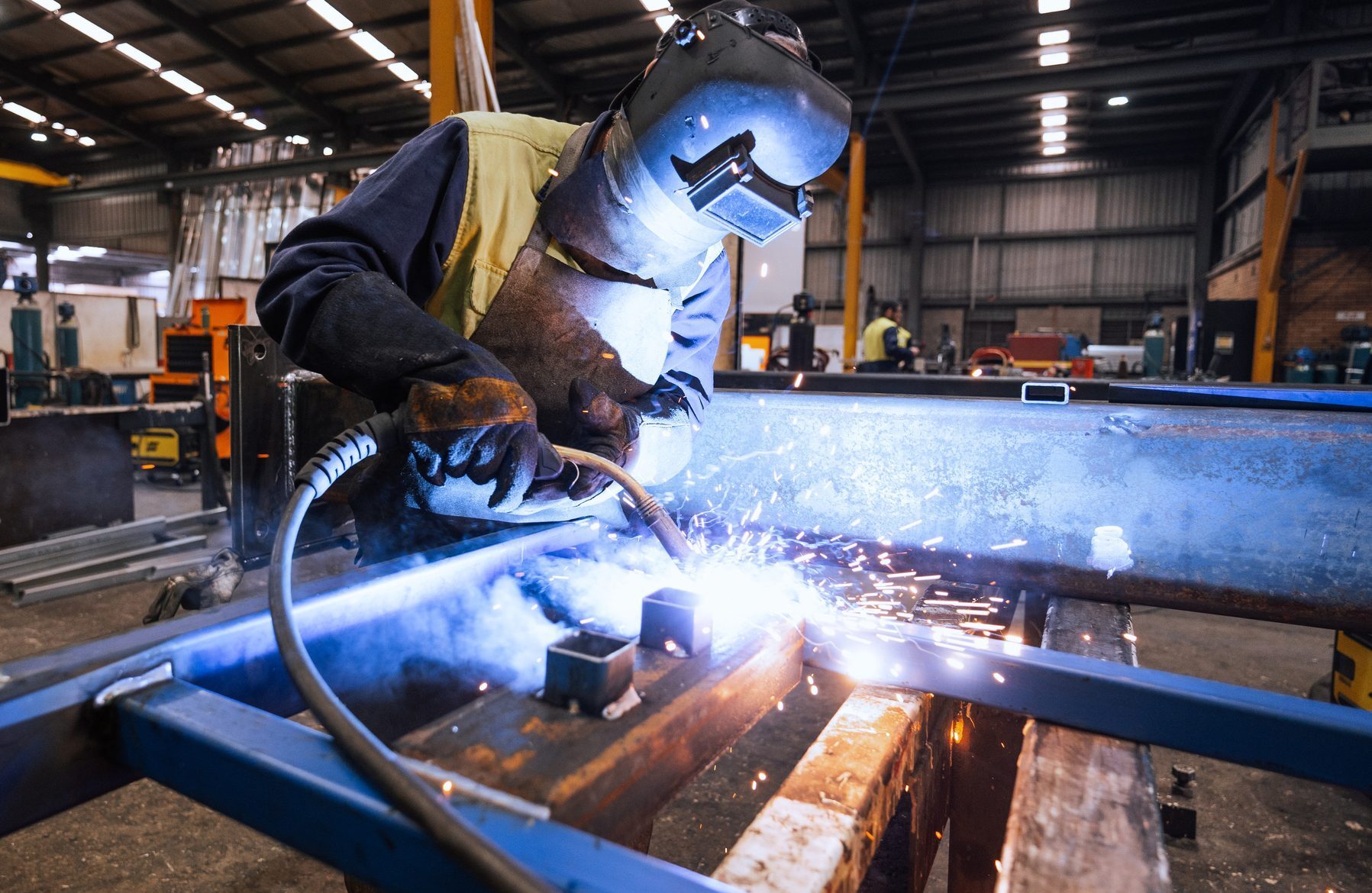 Worker in protective gear welding metal in an industrial factory setting with sparks flying around brightly illuminating the area
